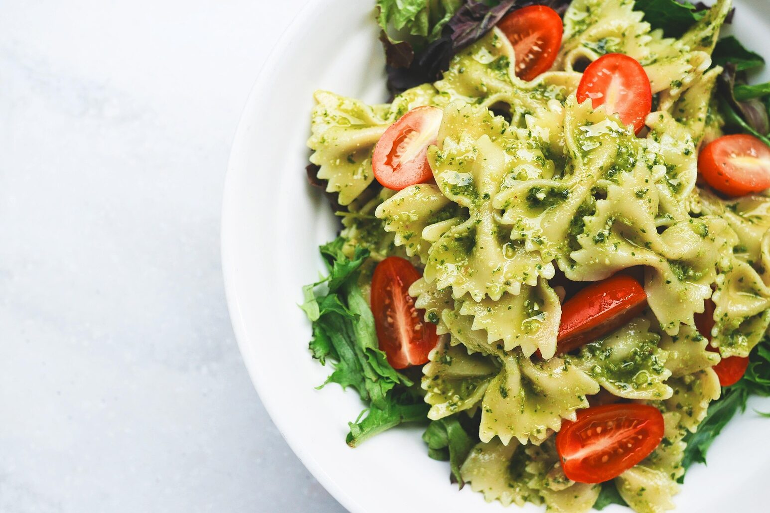 A plate of pasta, fresh tomatoes and green pesto