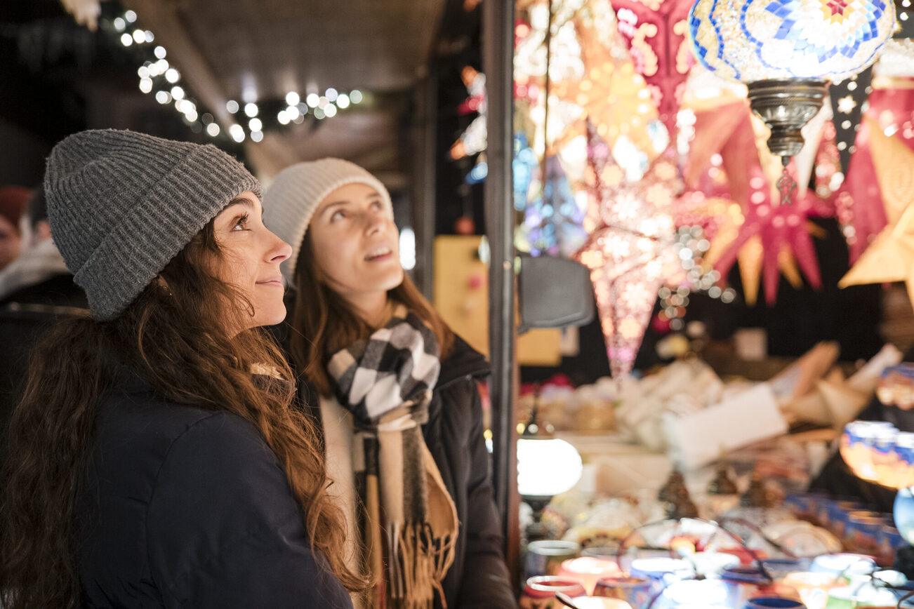 Zwei junge Frauen schauen an einem Stand bunte Sternlampen an.