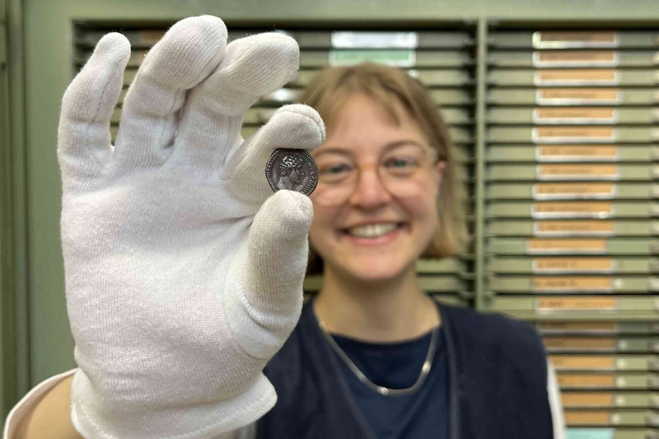 Frau hält eine Münze des Mainzer Münzkabinetts in die Kamera