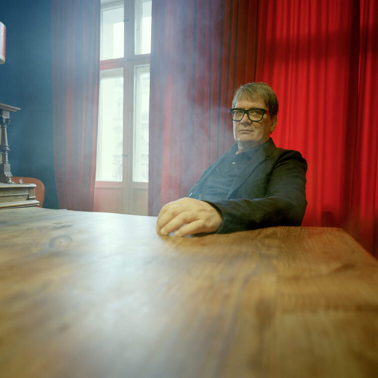 The author Sven Regener sitting at a table with red curtains behind him
