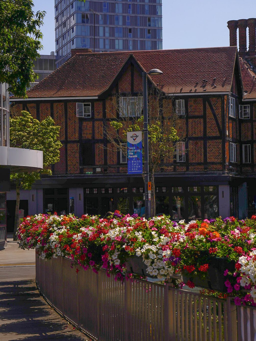 A bridge with flowers in front of a half-timbered house, with a skyscraper in the background