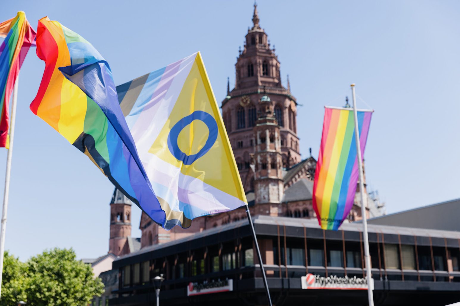 Die Regenbogenflagge sowie die Progressflagge im Wind wehend vor dem Mainzer Dom
