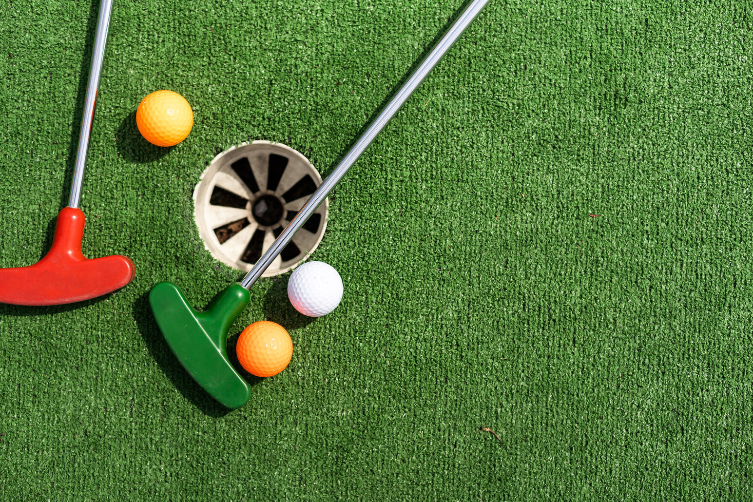 Roter und grüner Minigolfschläger mit drei Golfbällen liegen auf Kunstrasen