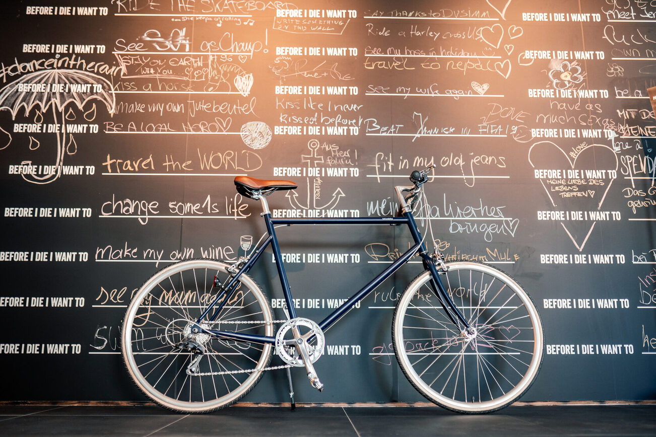 Un vélo est placé devant un mur avec des phrases "Before I die".