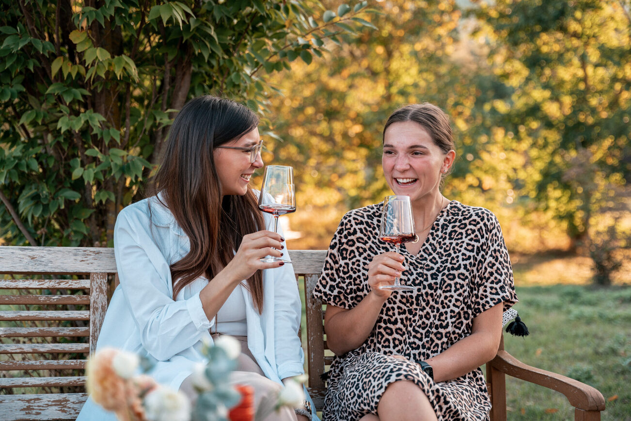 Zwei Frauen sitzen mit einem Glas Wein auf einer Bank.