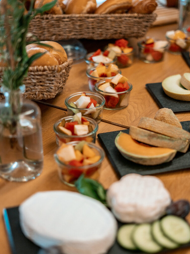 Käse, Gurken, Tomaten, Brötchen und vieles mehr auf einem Tisch.