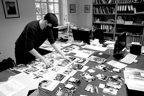 Ein Mitarbeiter des Archivs mit Mundschutz vor einem Tisch voller Fotos.