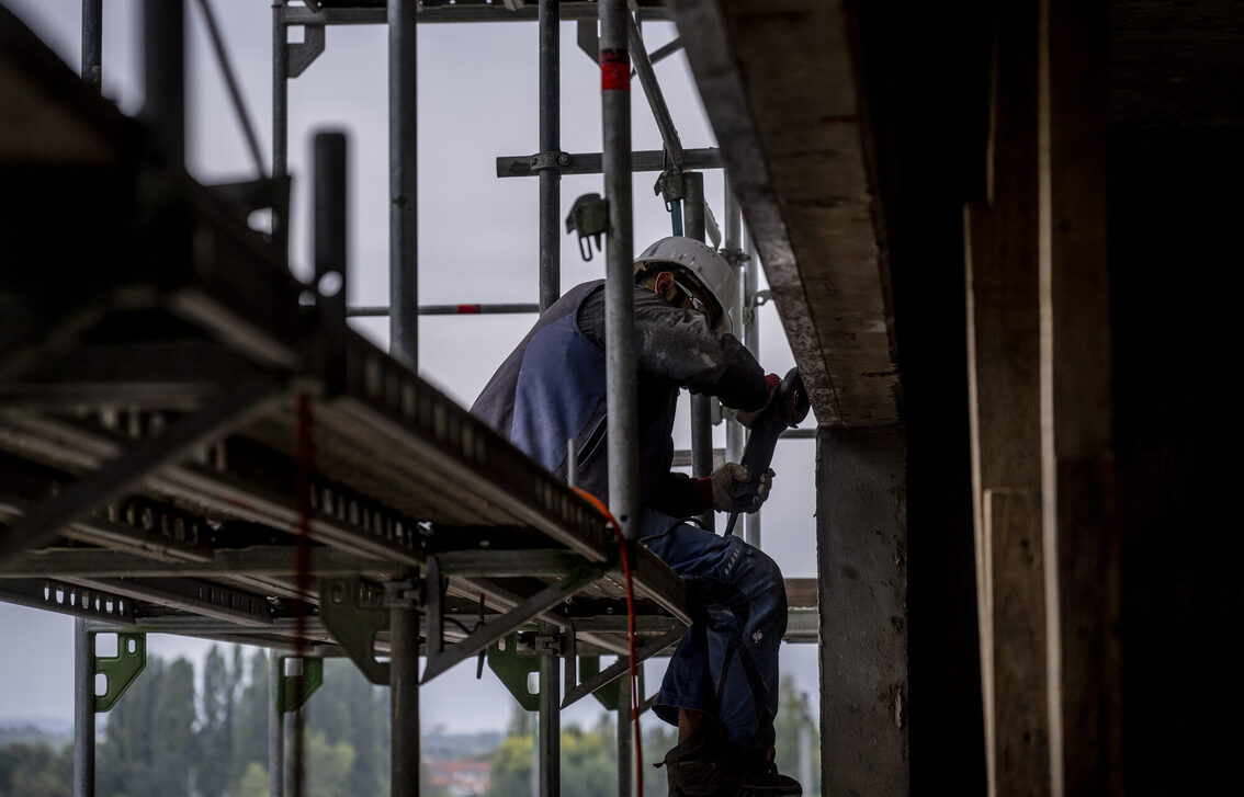Un operaio edile siede su un'impalcatura e lavora alla facciata.