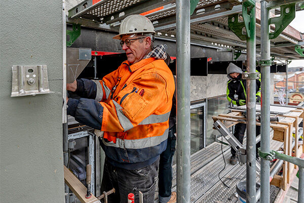 Zwei Bauarbeiter stehen auf einem Gerüst und arbeiten an der Fassade des Rathauses
