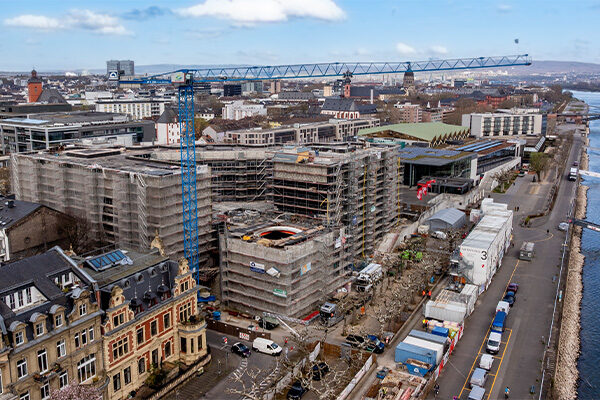 Drohnenbild der Rathausbaustelle mit Kran, rechts die Container und das Rheinufer.