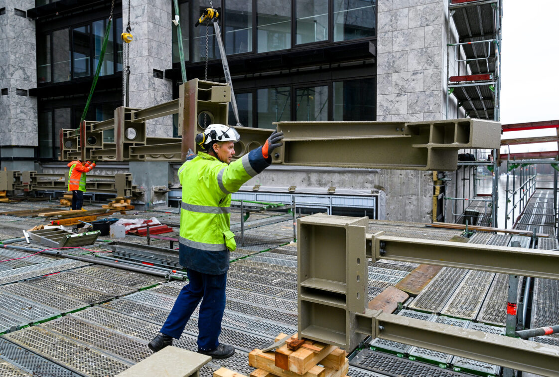 Bauarbeiter nehmen Stahlbauteil entgegen auf der Rathausbaustelle