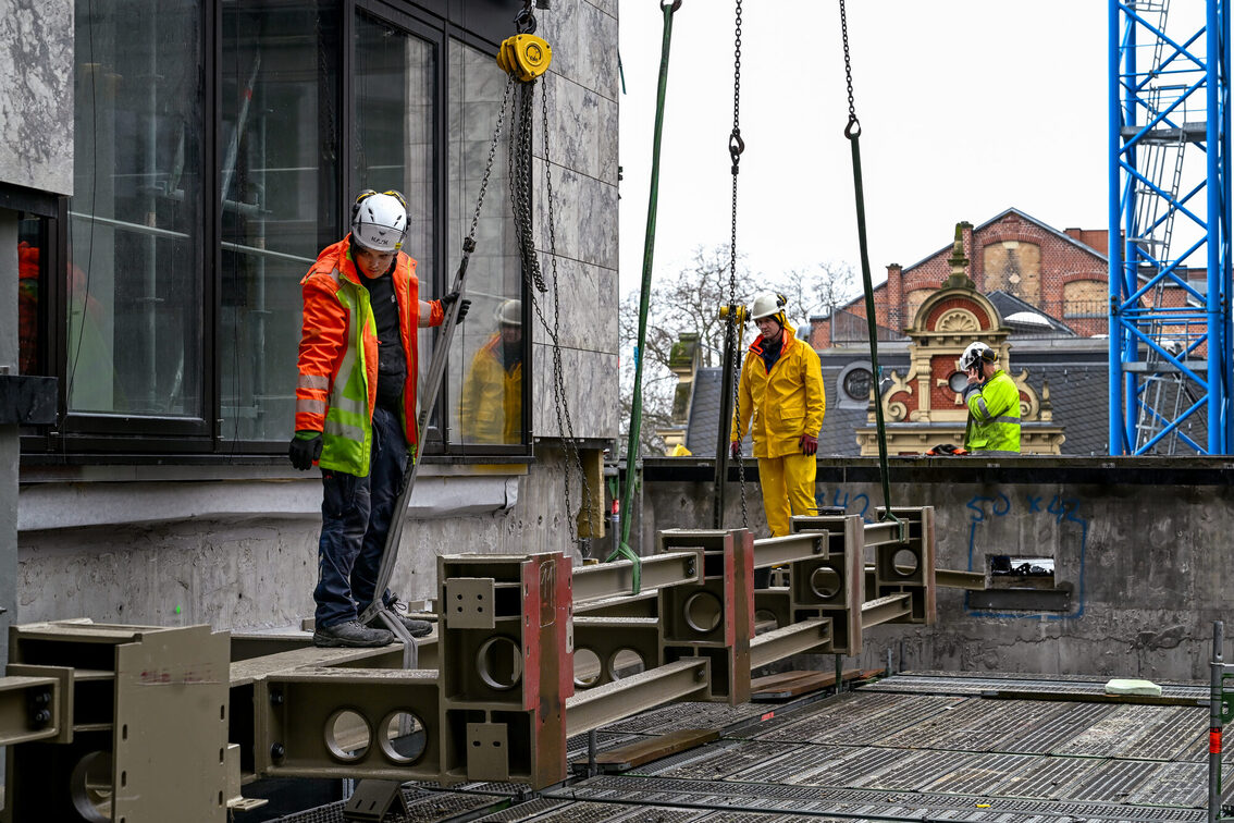 Bauarbeiter auf der Rathausbaustelle verlegen ein Stahlbauteil
