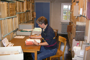 Eine Archivarin an einem Holztisch zwischen Regalen mit alten Büchern. © Stadtarchiv Mainz