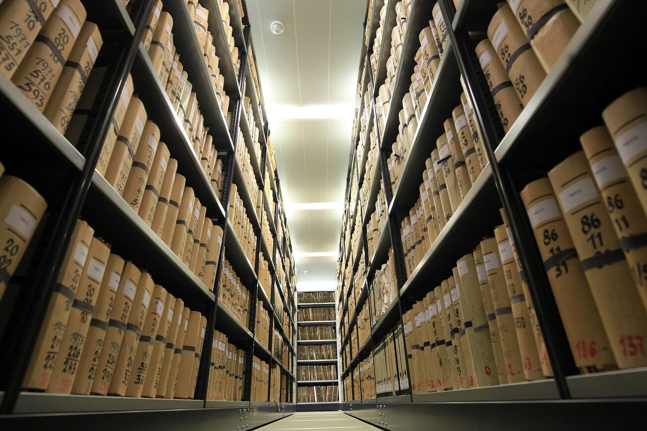 Blick in einen schmalen Gang, rechts und links Regale mit Aktenbündeln