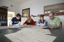 4 Personen an einem großen Tisch, auf dem sich große Pläne befinden