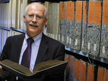 Prof. Dr. Wolfgang Dobras mit aufgeschlagenem Buch vor Archivregal