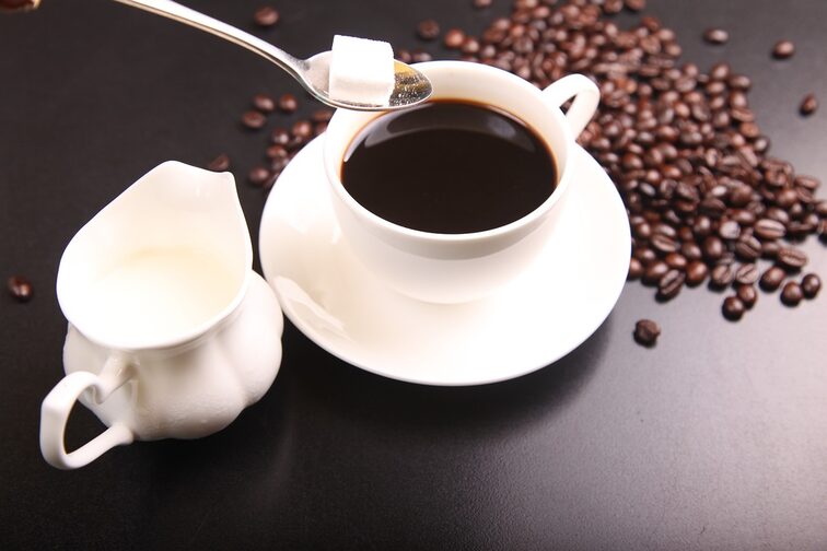 A cup of coffee with milk and sugar, coffee beans in the background