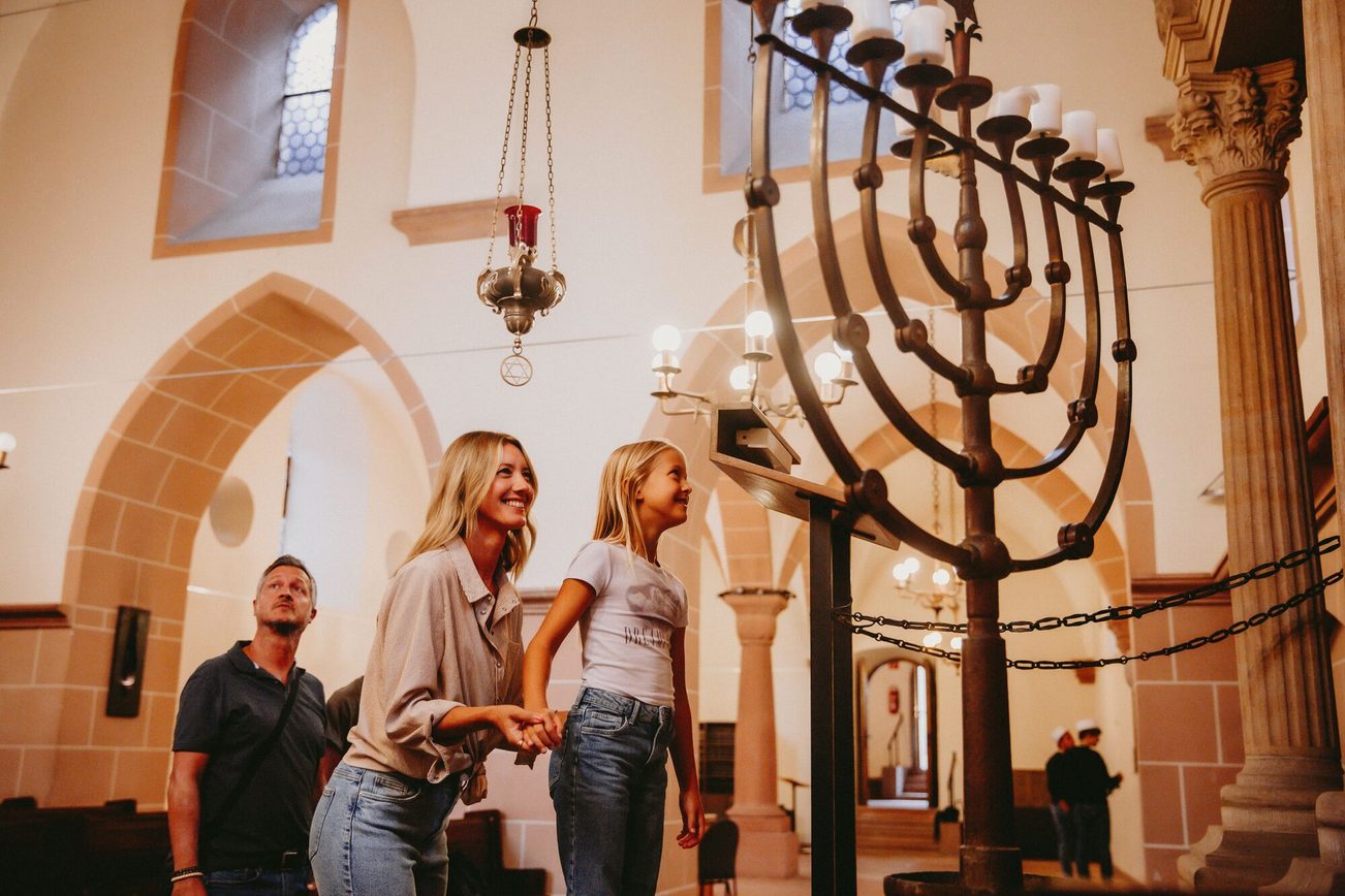 Three people in Worms synagogue: a man in the background, a woman with her daughter in the foreground. Looking at