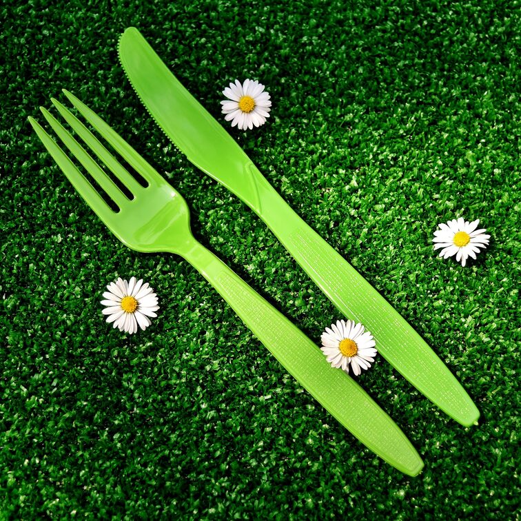 Couverts en plastique vert sur une pelouse artificielle avec des marguerites
