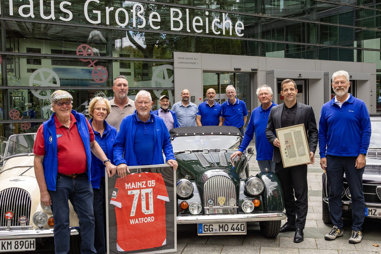 Menschengruppe steht vor Oldtimern und hält ein Mainz 05 Trikot hoch