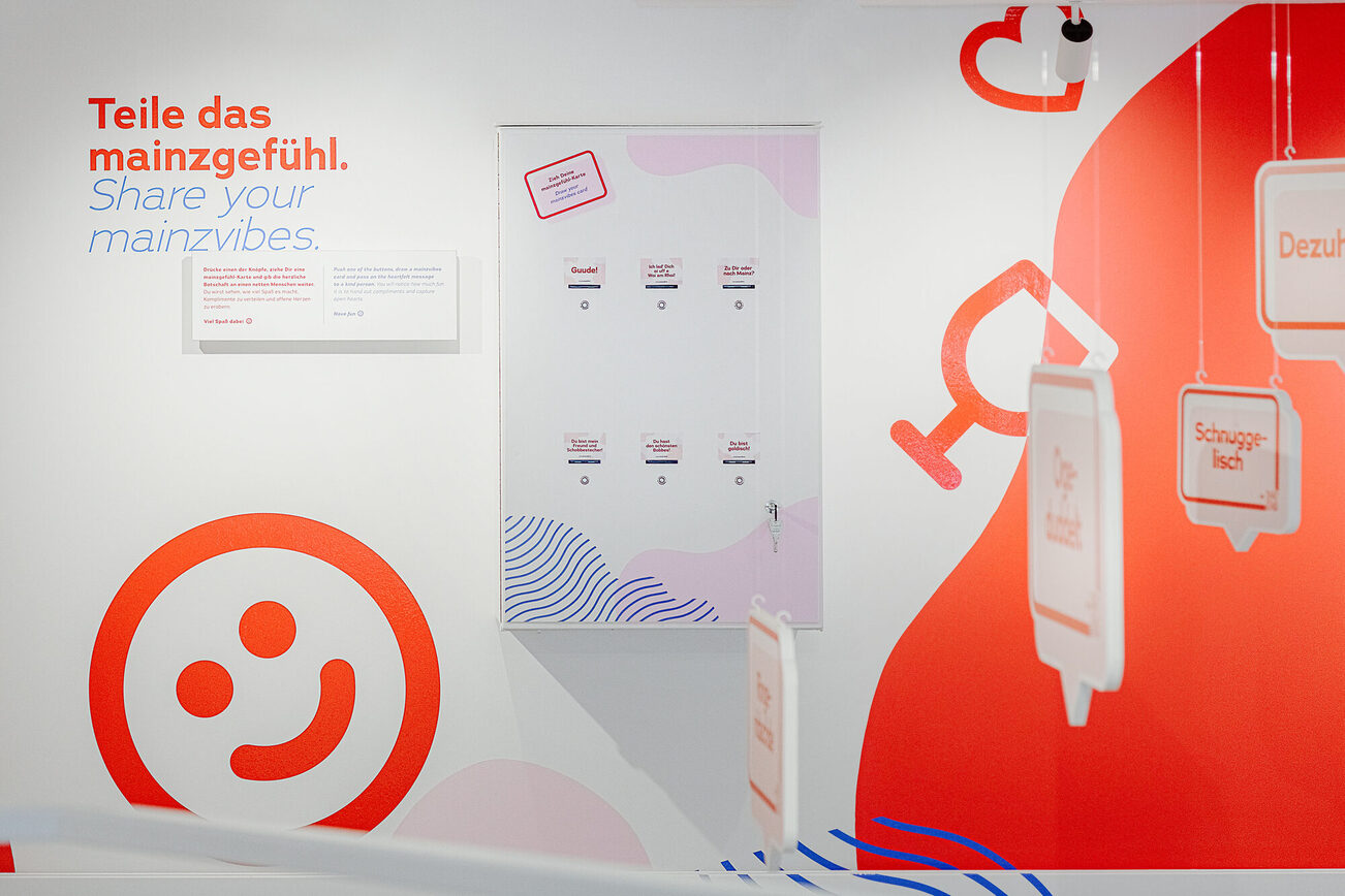 Wand: mainzgefühl im mainz STORE - weiß mit roten Icons: Smiley, Herz, Weinglas, Text: Teile das mainzgefühl.