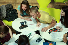 Mehrere Studierene sitzen zusammen an Tischen und diskutieren