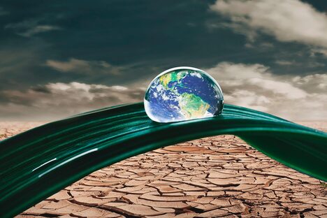 Bild der Weltkugel als Wassertropfen auf einem grünen Blatt in der Wüste