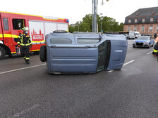 Auf der Seite liegendes Unfallfahrzeug mit Einsatzkräften im Hintergrund.