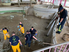 Einsatzkräfte entfernen Schlamm aus einem Schwimmbecken.