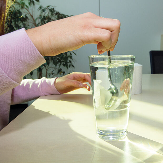 Ein Stück Toilettenpapier wird in einem Glas Wasser verrührt.