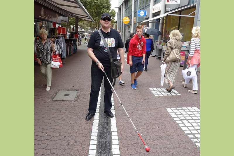Mann mit Taststock geht entlang der taktilen Leitlinie in der Innenstadt.