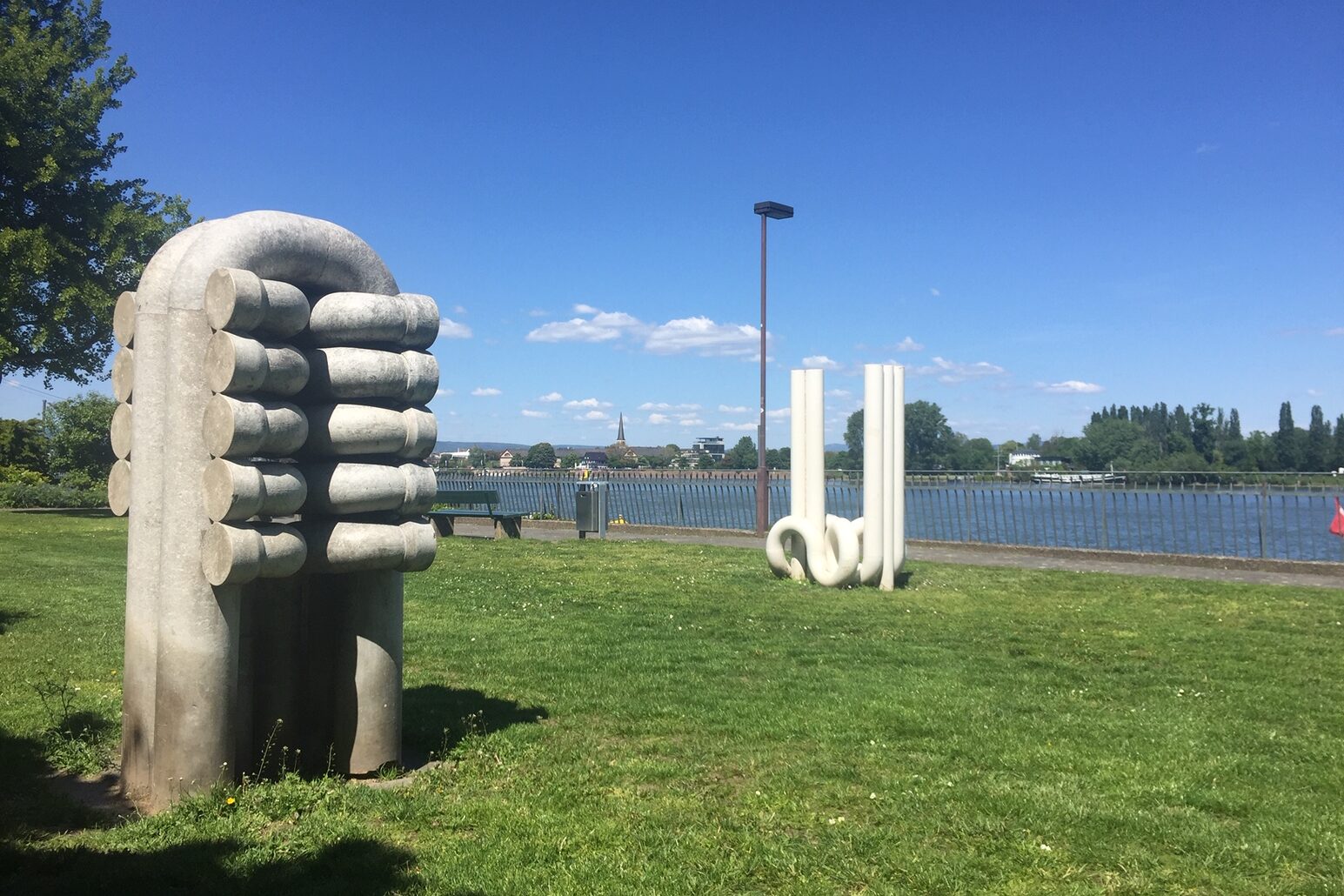 Zwei Kunstwerke auf einer Wiese, im Hintergrund der Rhein.