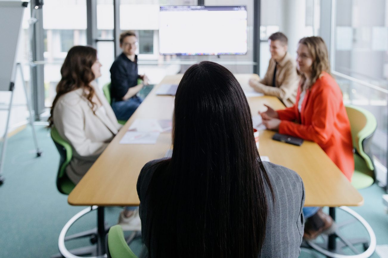 Five young employees are sitting at a table, with a screen in the background.