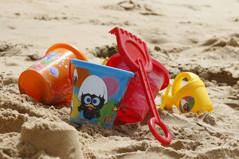 Three colorful toy buckets, a red children's shovel, and a children's watering can are lying in the soft sand.
