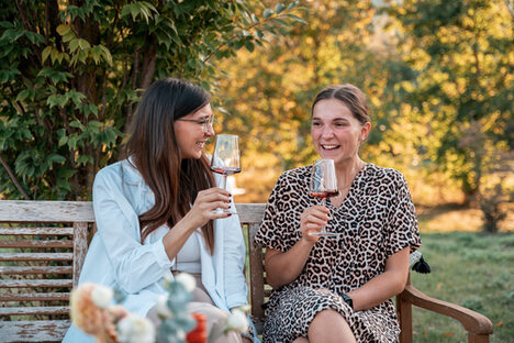 Zwei Frauen sitzen mit einem Glas Wein auf einer Bank.