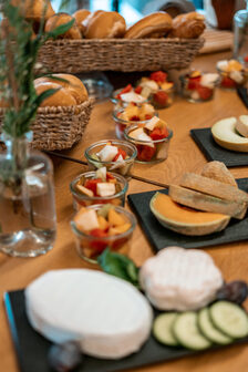 Käse, Gurken, Tomaten, Brötchen und vieles mehr auf einem Tisch.