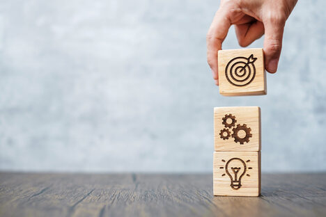 Eine Hand stapelt Holzwürfel mit Eingravierungen einer Glühbirne, Zahnränd